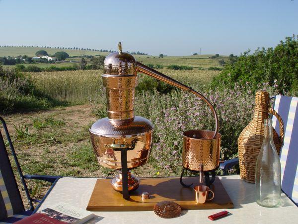 Das Bld zeigt eine Arabia destille im Freien auf einem Klapptisch - hier wierden im Freien ätherische Öle destilliert. Das Destillatio Buch liegt auch dabei